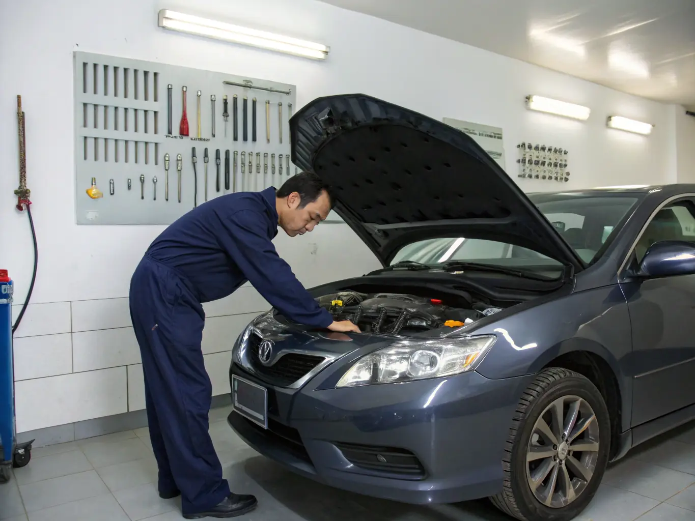 A mechanic performing a detailed inspection of a car engine in a clean and organized auto repair shop, focusing on the various components and their condition.